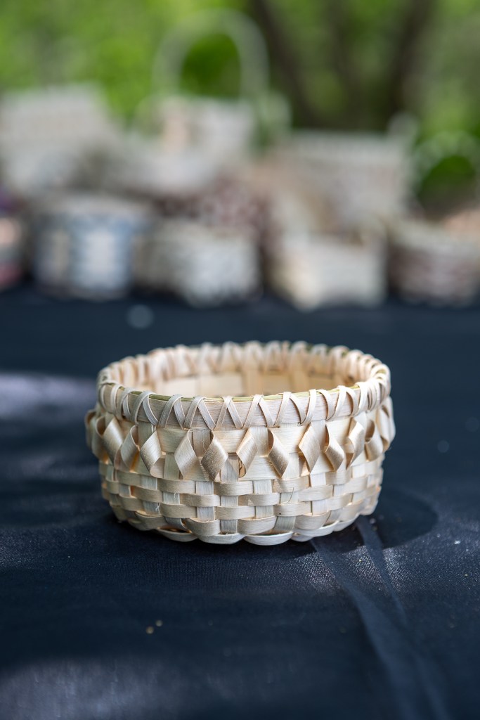 A handcrafted woven basket made of natural materials, displayed on a black table, with additional baskets blurred in the background.