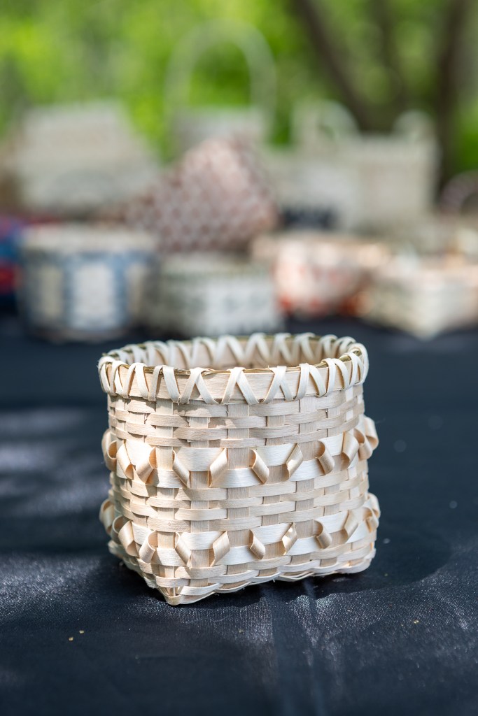 A close-up of a handmade woven basket, featuring intricate patterns and a natural light finish, set against a blurred background of additional baskets.