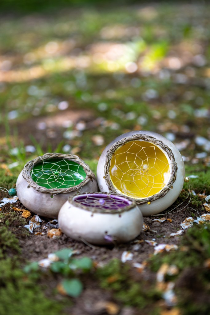 Three handmade pottery pieces with colorful interiors (green, yellow, and purple) displayed on a nature background.