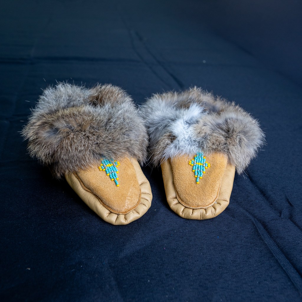A pair of handmade Mi'kmaq moccasins featuring a fur trim and intricate beaded designs on a leather surface.