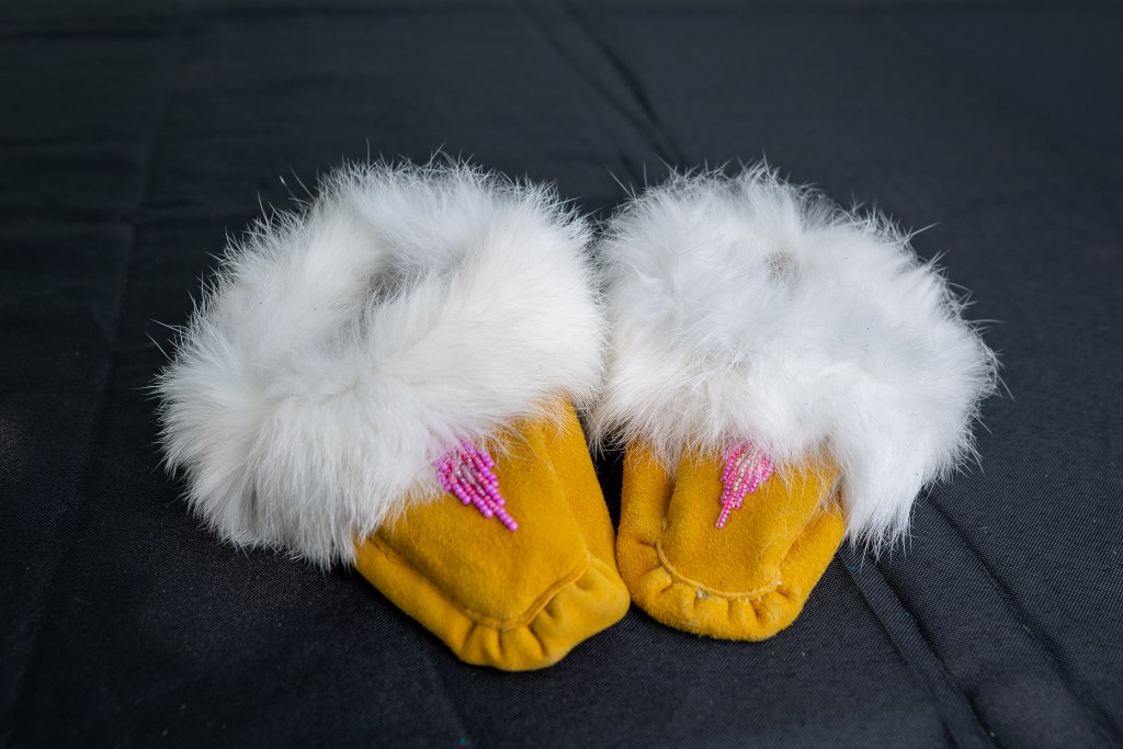 A pair of traditional Mi'kmaq moccasins featuring a soft yellow exterior and white fur trim, adorned with pink beadwork.