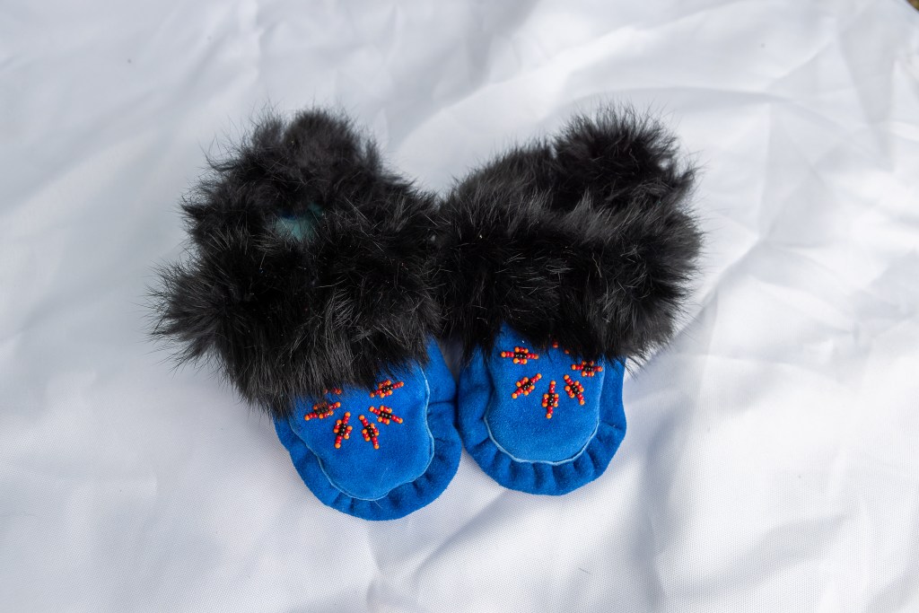 A pair of handmade blue moccasins with fur trim and decorative beadwork displayed on a white background.